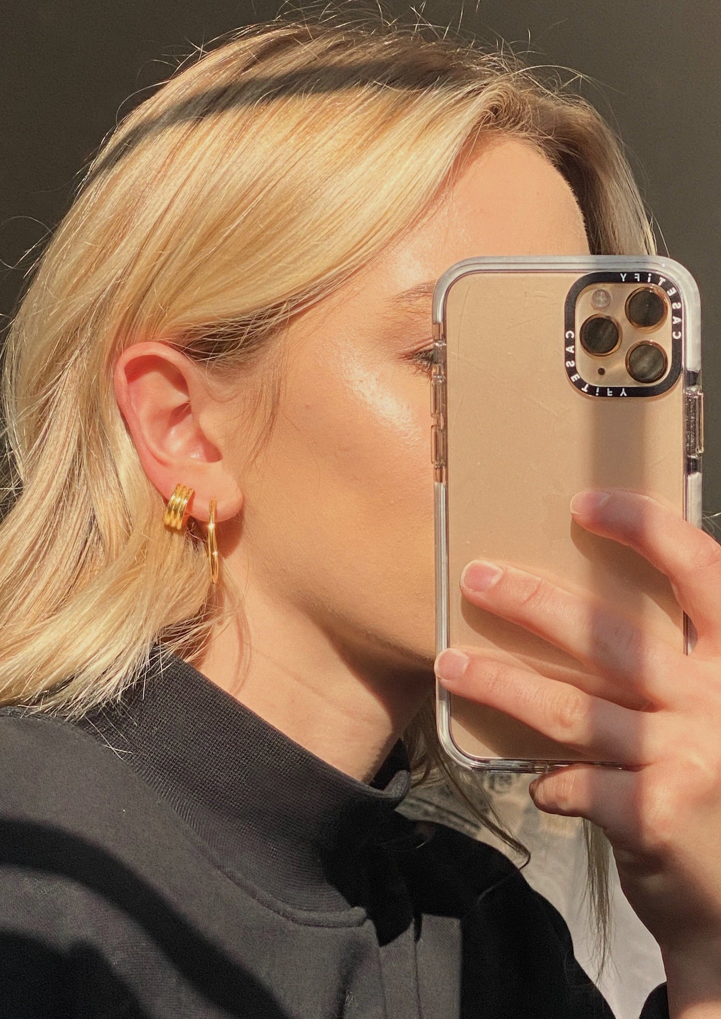 A model is wearing the small hoops and a bigger set of hoops. Both earring pairs are in gold. The model is posing in a golden sunlight.