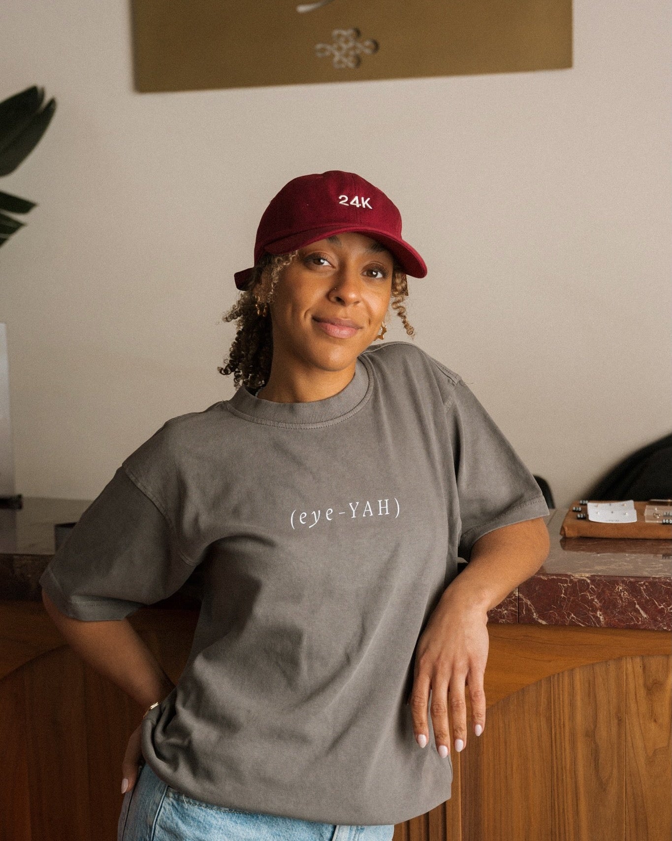 Person wearing a gray t-shirt with text and a red cap indoors.