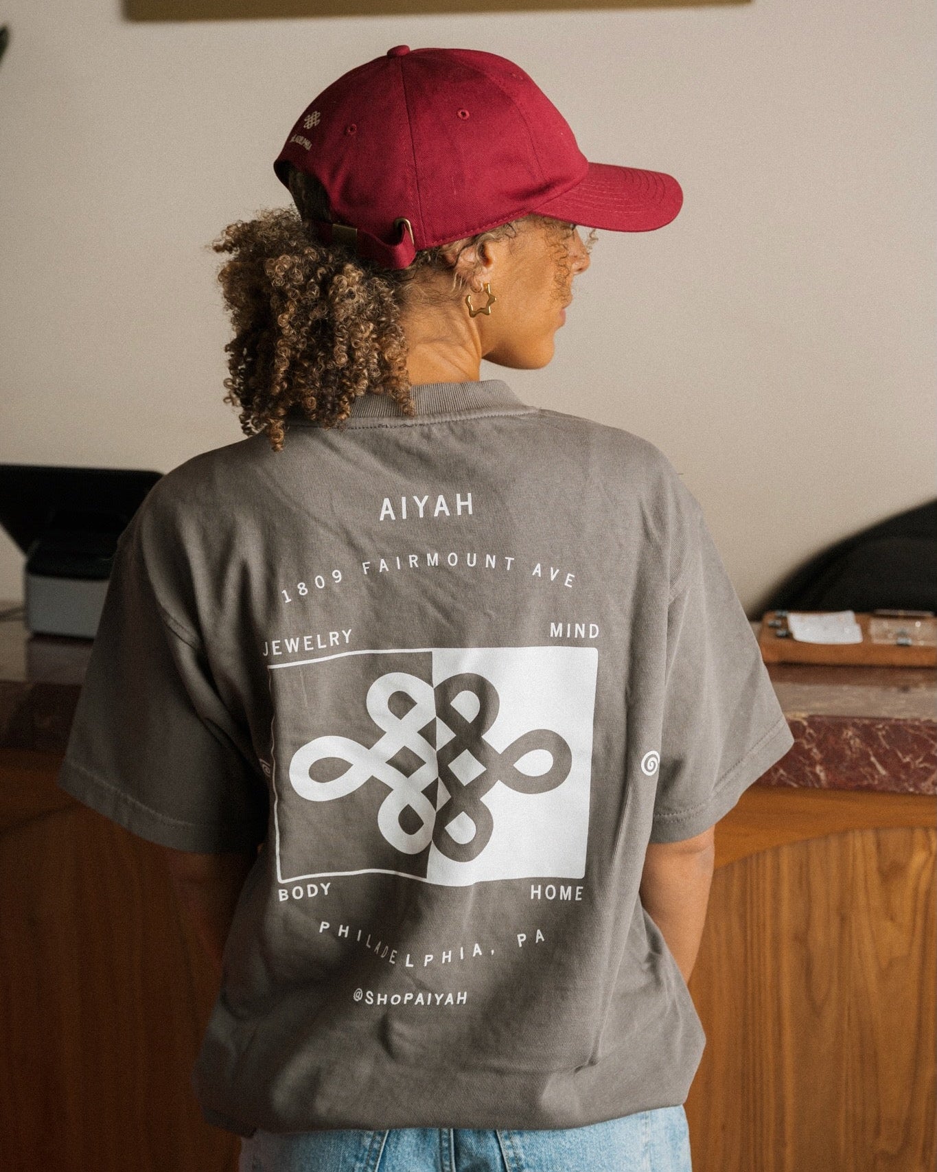 Person wearing a gray t-shirt with a logo and text, facing away from the camera.
