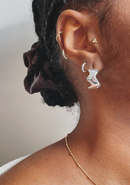 The model is wearing three pairs of smooth Ear Huggers in Silver. She is also wearing the Wave Hoops in silver. 
