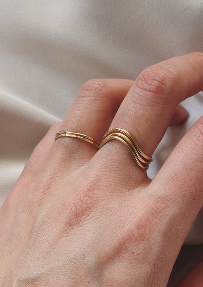 A model is wearing three gold Curve Rings on her middle finger. She is also wearing two gold Simple Stacking Rings on her ring finger. This is a lifestyle photo of the Curve Ring.