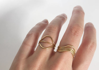 The model is wearing two Curve Rings and a Simple Stacking Ring on her ring finger. She's also wearing three curve rings sitting in the same way on her middle finger. All of the rings are gold.