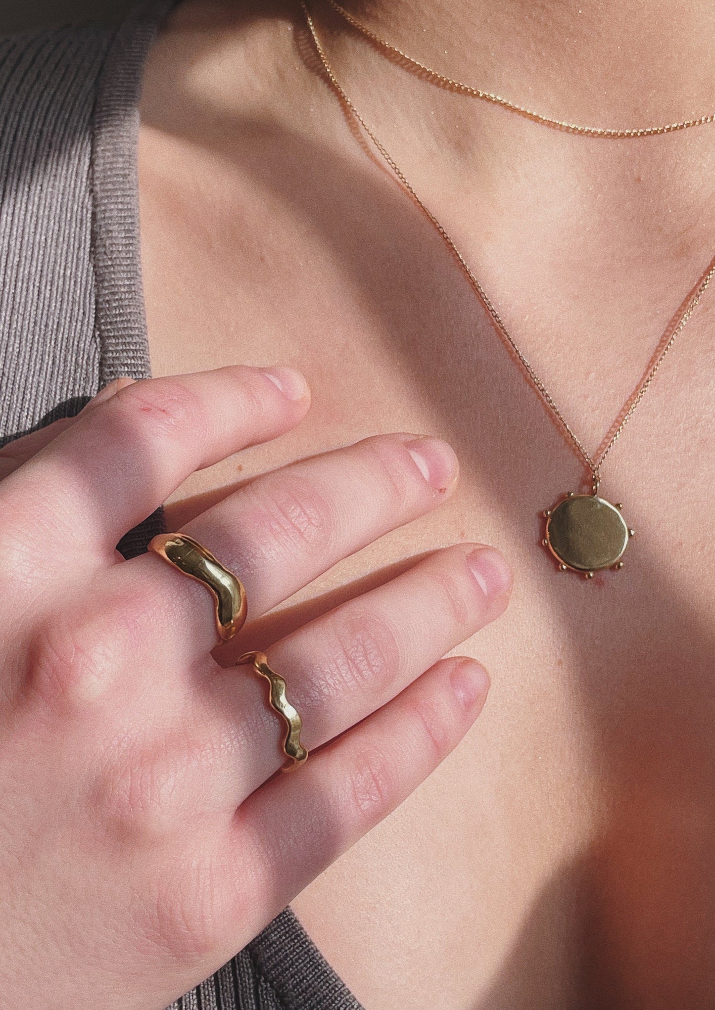 A model is wearing the Organic Ring, Squiggle Ring, and Vision Necklace. All of the jewelry is gold. 